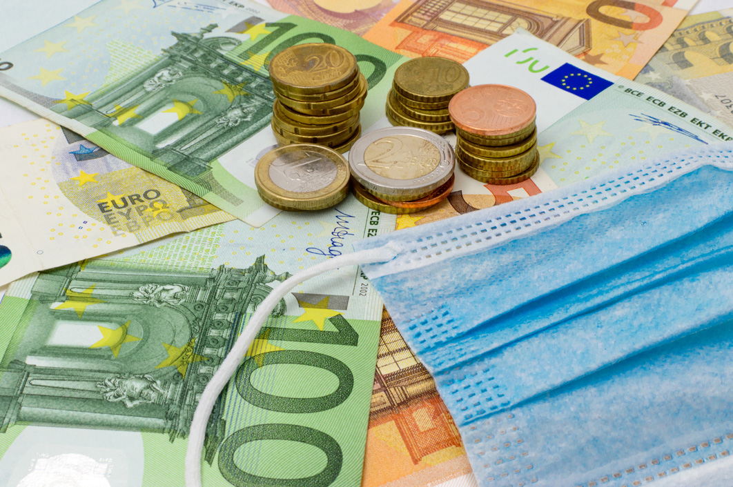 Moedas, notas e máscara cirúrgica. Impacto financeiro da Covid-19.