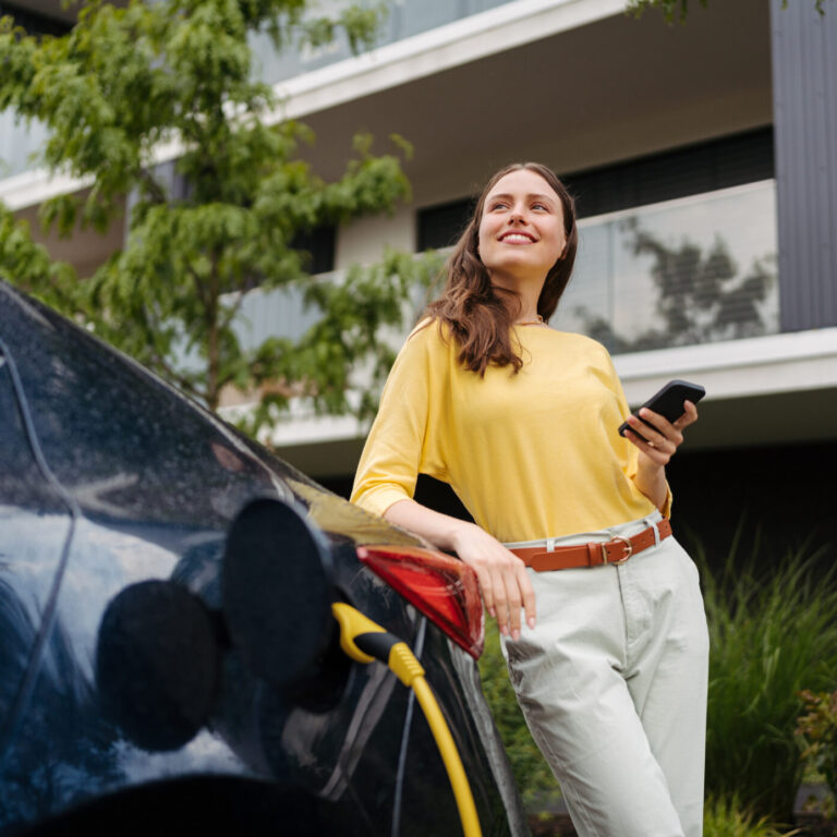 Mulher jovem junto a um carro elétrico que está a ser carregado