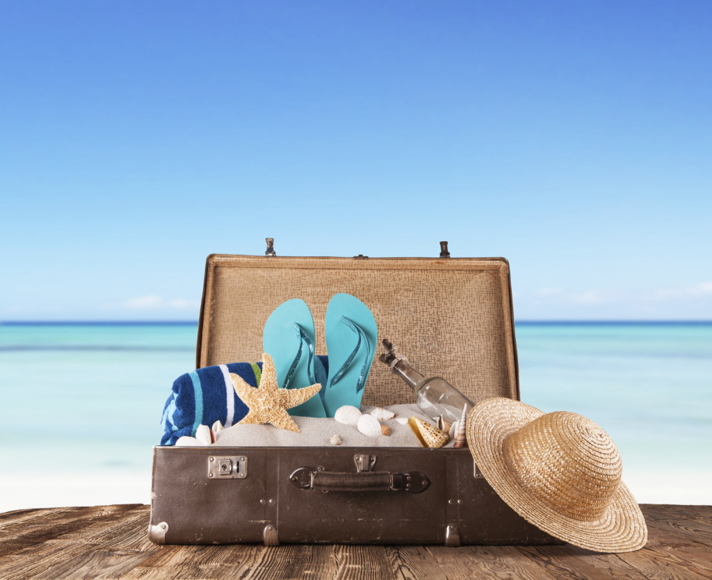 Concept of summer travelling with old suitcase and accessories. Blur beach on background